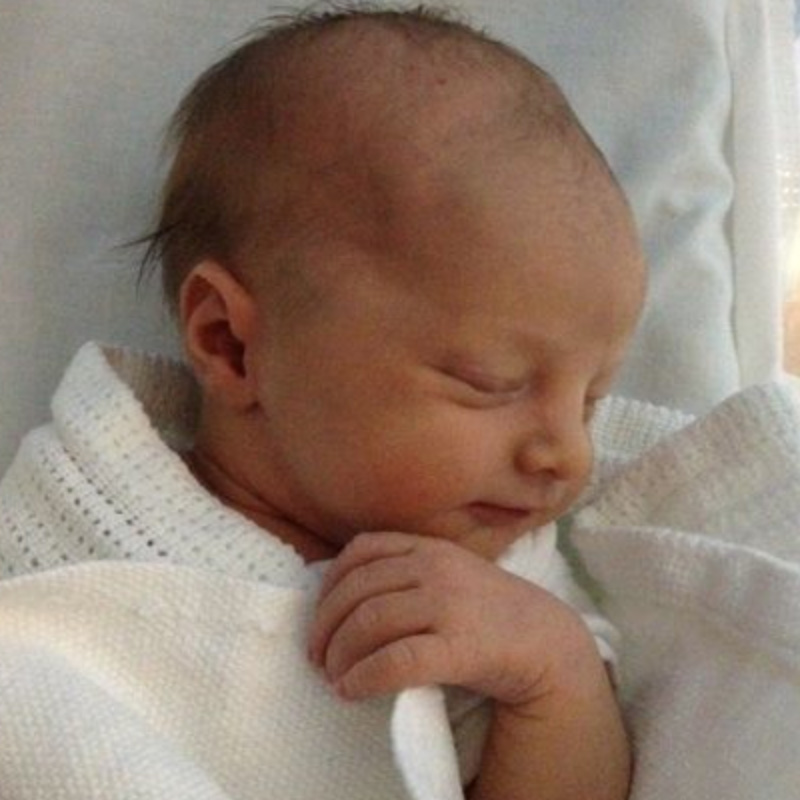 Newborn Joseph Lewthwaite, eyes closed clutching blanket with one hand.